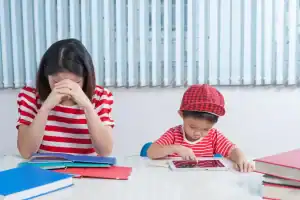 Asian boy playing on a tablet; his mother is frustrated